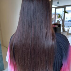 Back view of a person with long straight brown hair with a subtle purple tint wearing a pink to purple gradient garment indoors