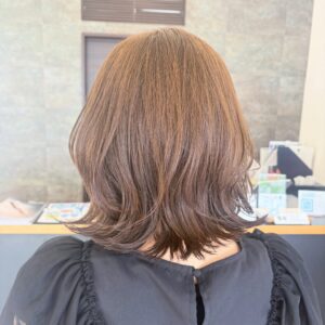 Back view of a person with shoulder length brown hair wearing a dark ruffled blouse inside a shop or salon