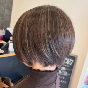Back view of a person with a short, rounded brown bob with light blonde highlights in a hair salon setting.