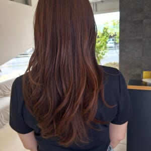 Back view of a person with long reddish brown hair in a black top inside a bright indoor space