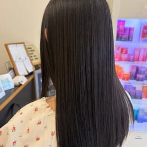 Back view of a person with long straight glossy black hair in a floral blouse at a salon