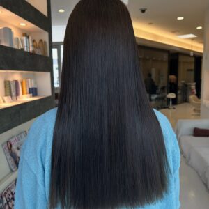 Back view of a person with long straight black hair wearing a blue top inside a hair salon