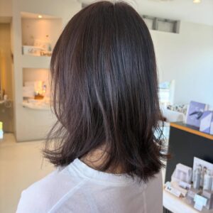 Back view of a person with shoulderlength dark brown hair in a bright salon setting