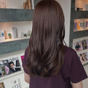 Person with long brown hair viewed from behind wearing a dark purple shirt standing in a magazine shop or salon display area