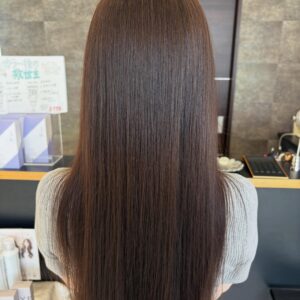 Back view of a person with long straight brown hair in a hair salon setting
