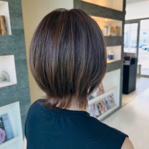 Back view of a person with a sleek short brown bob haircut in a modern salon with magazines on lower shelves and warm lighting