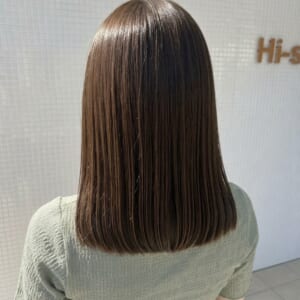 Back view of a person with straight shoulder length brown hair in a light green textured top standing in a tiled interior