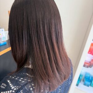 Person seen from behind with straight dark brown hair and a blue knit sweater standing near store shelves in a shop setting